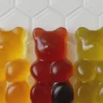 Colorful homemade gummy bears in a glass bowl with gummy bear molds and fresh ingredients.