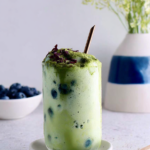 Delicious matcha frappuccino with blueberry swirl and whipped cream topping served in a clear glass.