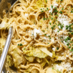 Bowl of melty cabbage pasta carbonara with parsley and Pecorino Romano, rustic wooden table setting.