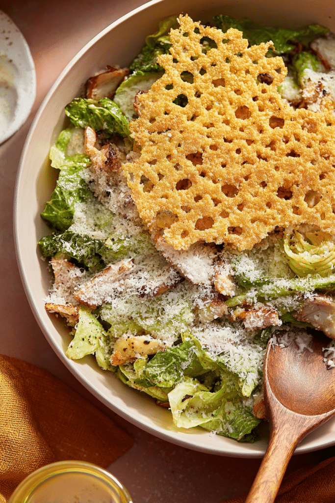 Micro chop caesar salad with grilled chicken, croutons, and a giant parmesan crisp in a white bowl.