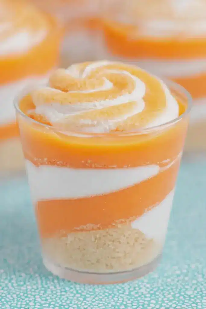 Close-up view of orange creamsicle cups with shortbread crust, orange fluff pudding, and whipped topping.