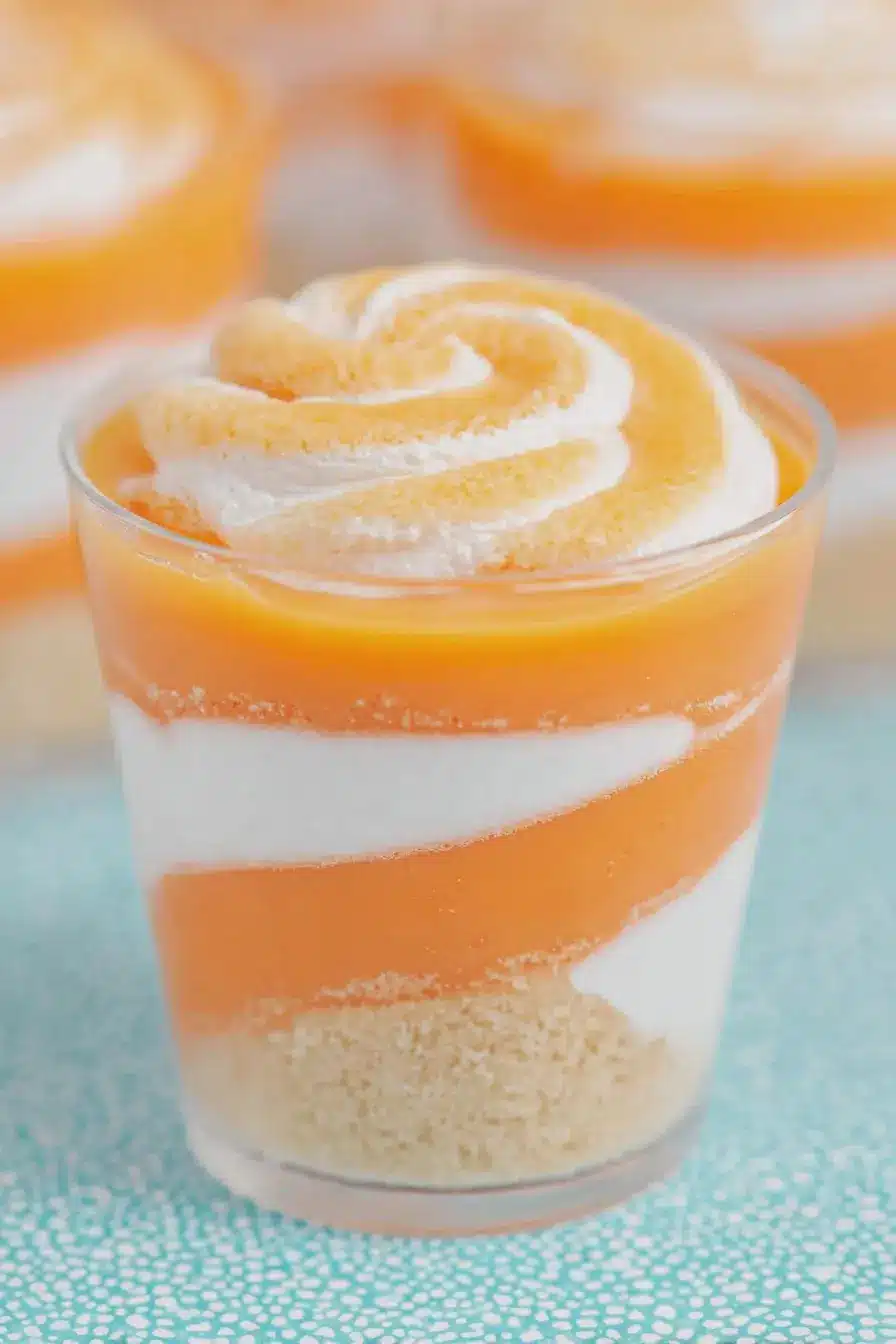 Close-up view of orange creamsicle cups with shortbread crust, orange fluff pudding, and whipped topping.