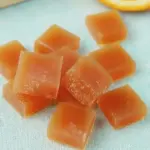 A colorful arrangement of orange-honey fruit snacks alongside fresh oranges and a honey jar, highlighting the healthy ingredients used.