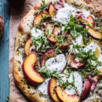 Slice of peach and burrata pizza with fresh basil on a wooden board.