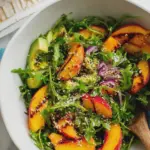 Vibrant peach and avocado salad with arugula, sliced almonds, and blue cheese in a bowl.