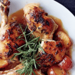 Roast chicken with plums, honey and rosemary on a rustic wooden table, showcasing the vibrant colors of the ingredients.