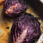 Roasted red cabbage drizzled with balsamic vinegar on a wooden table with herbs.