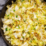 Close-up of sautéed cabbage with lemon zest and garlic garnish on rustic table.