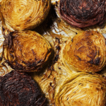 Grilled smoked cabbage steaks with a golden brown crust on a wooden board, garnished with herbs.