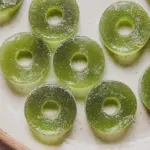 Homemade sour apple ring gummies on a wooden table with fresh apples and sugar.