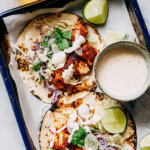 Close-up of spicy fish taco with cabbage slaw and lime crema on a wooden table.