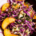 Colorful summer slaw with peaches and parsley in a bowl, garnished with sunflower seeds