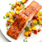 Plated sweet and spicy glazed salmon with peach and pepper relish garnished with fresh herbs.